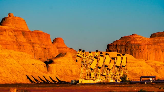 Line of pumpjacks against a stunning rocky landscape at sunset in Karamay, Xinjiang, China.