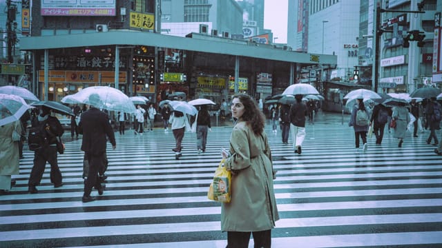 People with umbrellas cross at Shinjuku City in Tokyo on a rainy day.