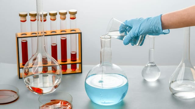 Close-up of scientist pouring liquid into a flask in a laboratory setting