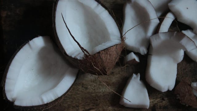 Rustic arrangement of fresh coconut halves and pieces on a dark wooden surface.