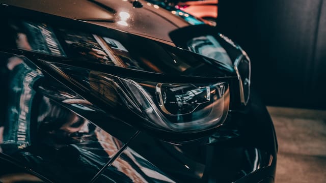 Close-up of a shiny black car's headlight in Munich, highlighting design and elegance.