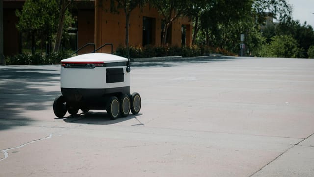 A sleek autonomous food delivery robot navigates a sunny urban landscape, showcasing modern innovation.
