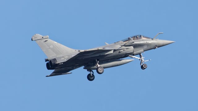 A sleek military jet flying high in the clear blue sky, showcasing aerodynamic design and power.