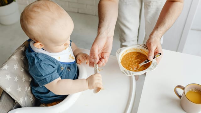A cute baby in a high chair being fed by a parent, creating a warm family moment.
