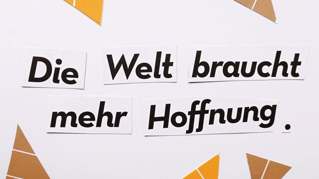 Inspirational text 'Die Welt braucht mehr Hoffnung' on a white background with triangle cutouts.