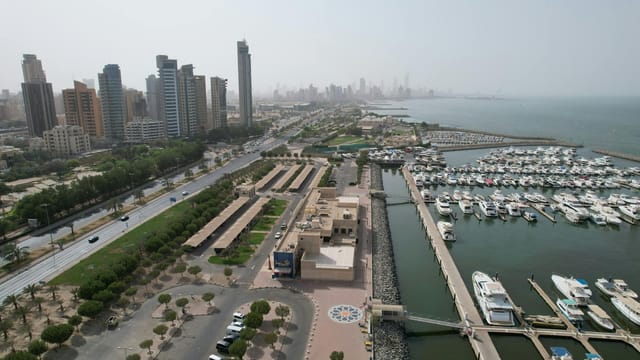 Aerial view of Kuwait City's modern skyline and bustling harbor with yachts.