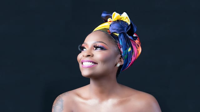 A beautiful portrait of a smiling woman wearing a vibrant headwrap, exuding joy and elegance.