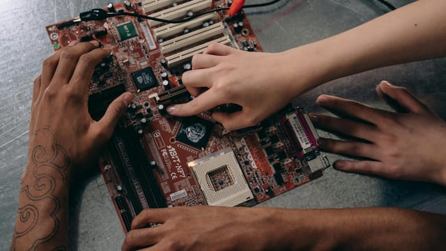Close-up of hands repairing a motherboard, highlighting teamwork and electronics engineering.