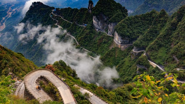 Breathtaking view of a winding road in Tianmen Mountain with lush green landscape and misty clouds.