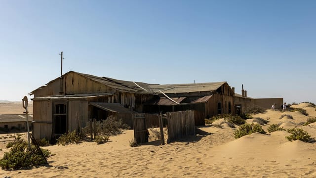 Rustic abandoned building in Namibia's desert landscape, surrounded by sand dunes.