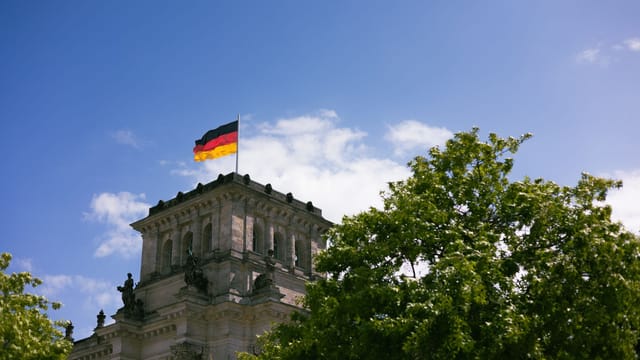 The iconic Reichstag in Berlin with the German flag flying high against a clear blue sky.
