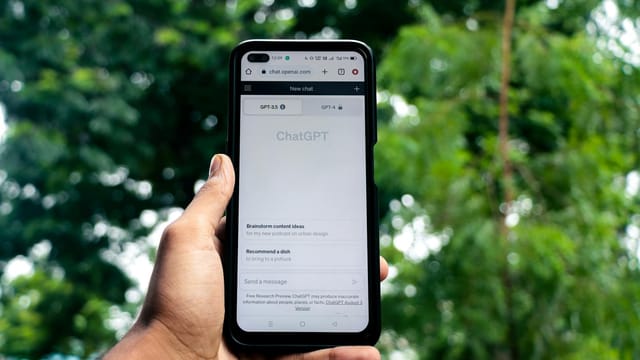 Close-up of a hand holding a smartphone displaying ChatGPT outdoors.