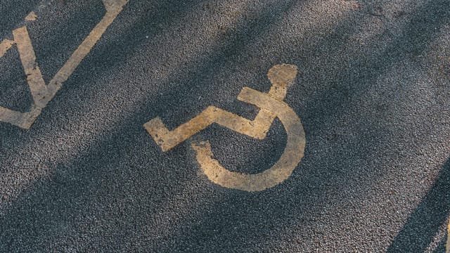 Close-up of an asphalt parking spot with a yellow wheelchair symbol for accessibility.
