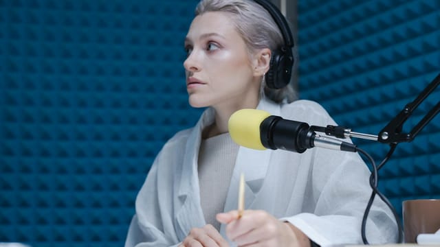 Confident woman wearing headphones hosting a podcast in a soundproof studio.