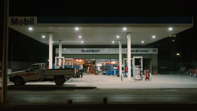A Mobil gas station with vehicles and people under bright lights at night.