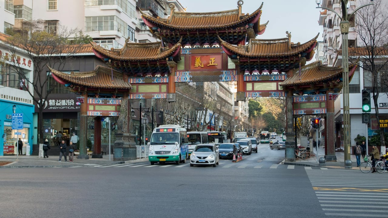A bustling street scene in Kunming with a traditional Chinese gate and modern cityscape.
