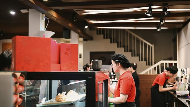 Baristas wearing red uniforms working in a bustling café, preparing beverages.