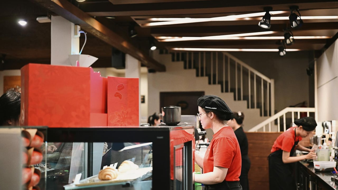 Baristas wearing red uniforms working in a bustling café, preparing beverages.