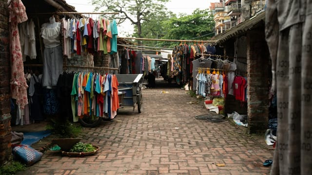 Outdoor market street showcasing vibrant clothing displays hanging in rows, ideal for commerce and tourism.