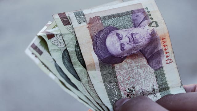 Detailed view of Iranian rial banknotes held in hand, illustrating finance and economy in Iran.