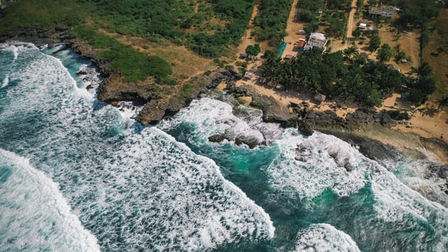 Stunning aerial photo showcasing Bolinao's rugged coastline with crashing waves and lush greenery.