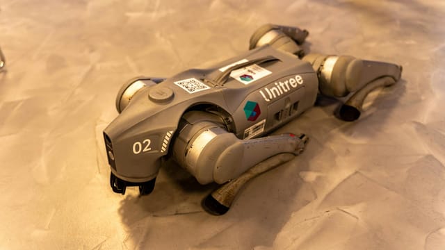 A Unitree robot dog resting on an indoor concrete floor.