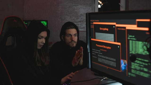 Cybersecurity experts in hoodies analyzing encrypted data on computer screens in an indoor setting.