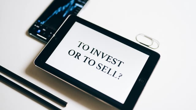 A tablet with text 'To Invest or To Sell?' on a white background.
