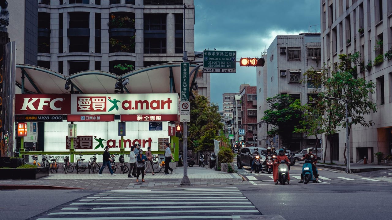 A bustling intersection with crosswalk, traffic lights, and people in an urban cityscape at night.