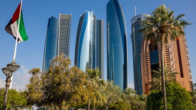 Captivating shot of the iconic Etihad Towers, Abu Dhabi landmark with palm trees and UAE flag.