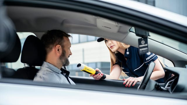 A police officer conducts a breathalyzer test on a male driver during a road safety check.