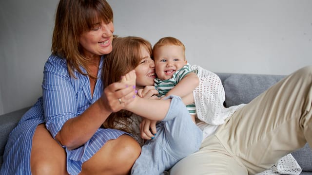 Happy grandmother with daughter and little boy resting on cozy couch in living room