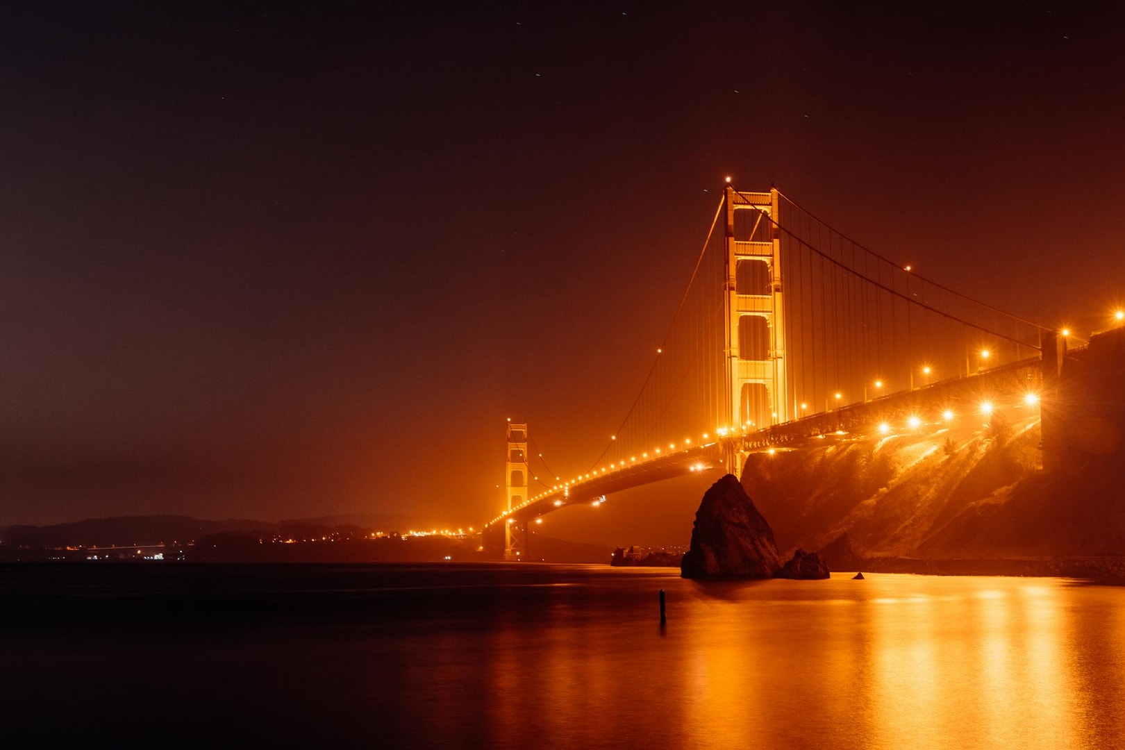 Stunning nighttime view of the Golden Gate Bridge glowing over calm waters in San Francisco.