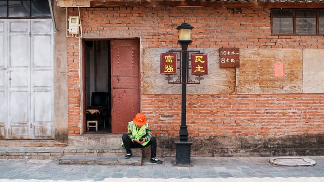 A construction worker in a reflective vest and helmet relaxing on a street during the day.