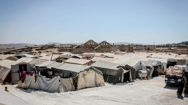 A refugee camp in Idlib, Syria, with tents under a clear blue sky, highlighting humanitarian aid efforts.