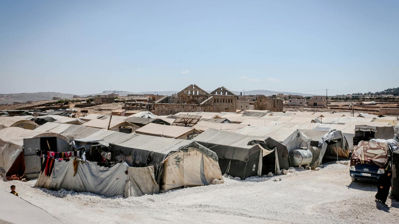 A refugee camp in Idlib, Syria, with tents under a clear blue sky, highlighting humanitarian aid efforts.