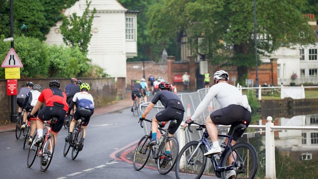 A group of cyclists enthusiastically participates in a charity bike event on a road surrounded by greenery.