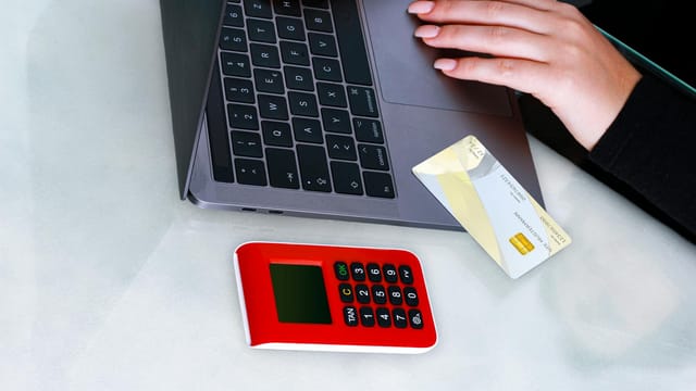 Hands using laptop with credit card and security device for online payment, emphasizing cybersecurity.