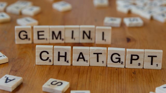 Close-up of wooden Scrabble tiles spelling Gemini and ChatGPT on a wooden surface.
