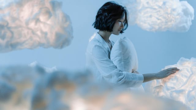 A serene scene of an Asian woman dreaming among soft, ethereal clouds.