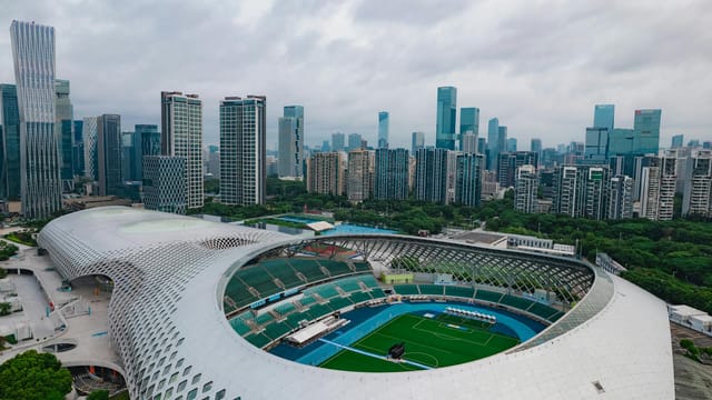 Stunning aerial shot of Shenzhen's modern stadium surrounded by skyscrapers, showcasing urban architecture and cityscape.