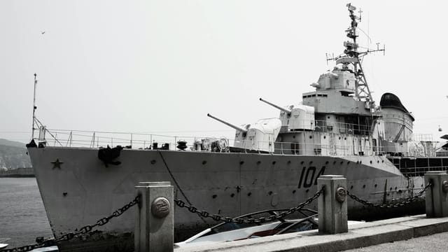A large naval destroyer ship docked at a harbor under a gray sky.