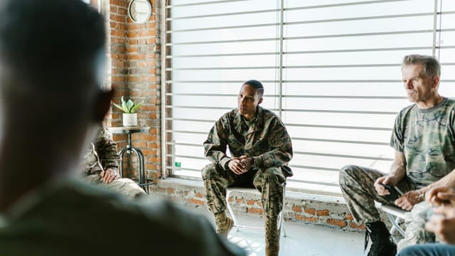 Military personnel participate in a supportive group therapy session indoors.