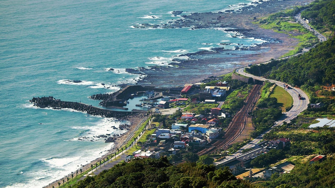 A stunning aerial shot of Taiwan's coastline, showcasing rocky shores, lush greenery, and a winding road along the ocean.