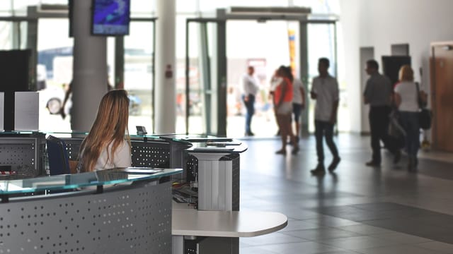 A bustling office reception area with people walking and a receptionist at a modern desk.