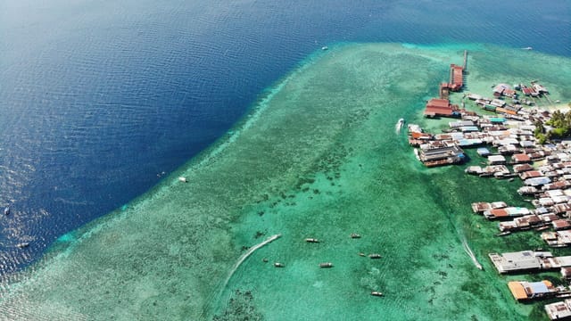 Boats floating on rippling endless sea near island with various residential houses in tropical country on summer day in nature
