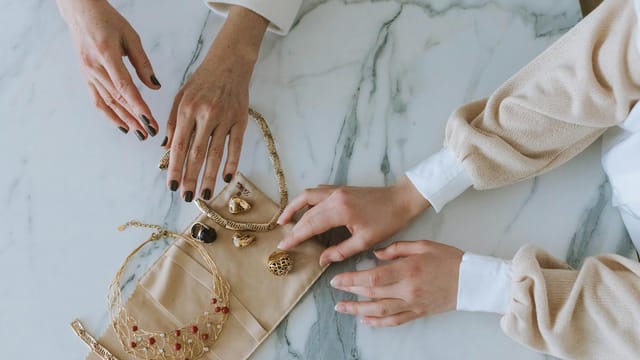 A sophisticated display of gold jewelry and hands on a marble surface, exuding luxury and elegance.