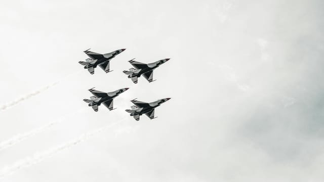 A squadron of fighter jets flying in formation against a cloudy sky.
