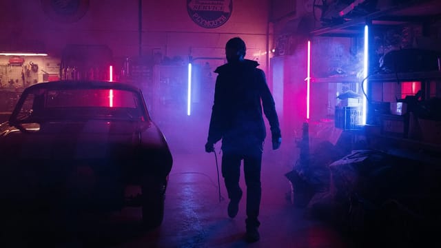A mechanic in a neon-lit garage works amidst vibrant pink and blue lights, creating a moody, cyberpunk atmosphere.