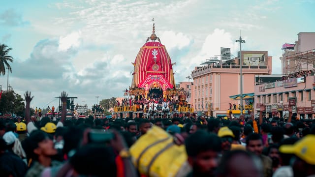 A colorful and lively street festival featuring a decorated chariot surrounded by a large crowd.
